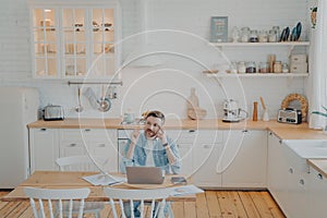 Young office worker working remotely from home with computer while sitting by kitchen table