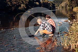 Young and old fisherman standing on the shore of lake with fishing rod. Father and son enjoy life. Men family, granddad