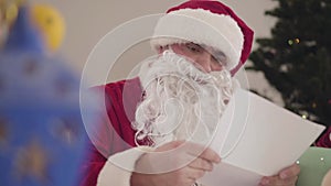 Young and old Santas examining letters on Christmas eve. Portrait of two men in red Christmas costumes reading wishes on