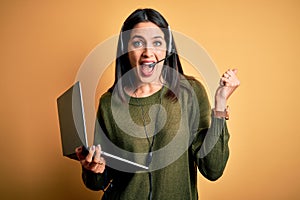 Young operator woman with blue eyes working on call center using computer laptop and headset screaming proud and celebrating