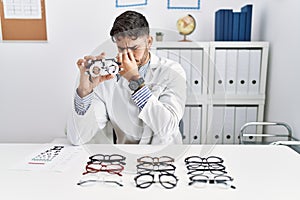 Young optician man holding optometry glasses tired rubbing nose and eyes feeling fatigue and headache