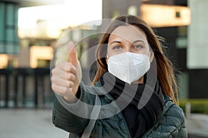 Young optimistic female student giving thumbs up gesture. She`s wearing a protective mask PPE to avoid air pollution or