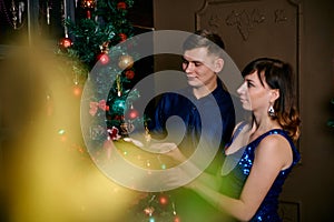Young ordinary family of two. Young husband and wife near christmas tree. Happy young hetero couple decorate christmas tree at
