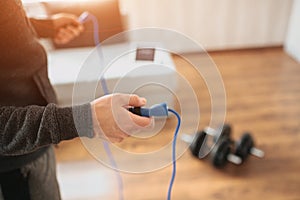 Young ordinary man go in for sport at home. Cut view and close up of workout beginner holding jump rope with both hands