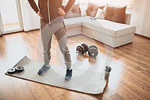 Young ordinary man go in for sport at home. Ordinary freshman in workout stand on mat and hold hands on hips. Cut view photo