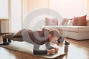 Young ordinary man go in for sport at home. Full size pictrue of freshman in workout and beginner guy stand in plank