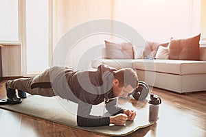 Young ordinary man go in for sport at home. Full size pictrue of freshman in workout and beginner guy stand in plank photo