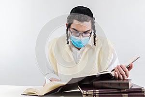 Young orthodox Jew with a face mask studying religious texts - concept of the new normal