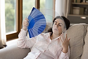 Young overheated woman use fan cooling herself resting at home