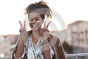 Young overjoyed african american girl with glitter on face showing peace sign and laughing