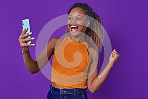 Young overjoyed African American woman holding mobile phone stands in studio