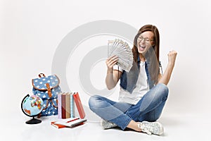 Young overjoyed woman student holding bundle lots of dollars, cash money do winner gesture, say Yes near globe backpack
