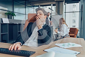 Young overtired businessman yawning while working inside modern office with computer photo