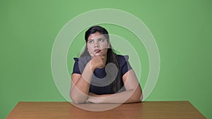 Young overweight beautiful Indian businesswoman against green background