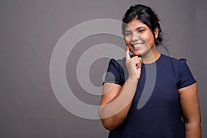 Young overweight beautiful Indian woman against gray background