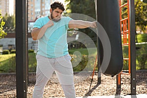 Young overweight man kicking heavy bag on ground