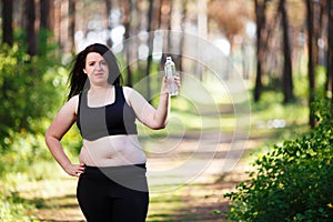 Young overweight smiling woman with a bottle of clear water outd