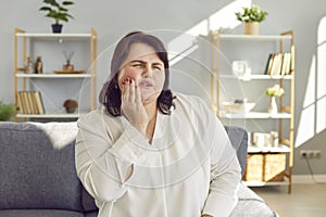 Young overweight woman suffering from toothache and holding her hand on her painful cheek