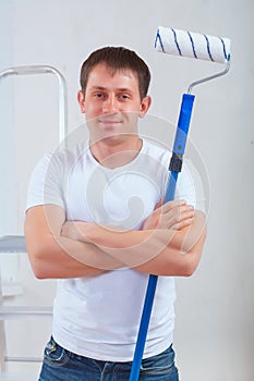 Young painter with crossed arms holding paintroller and looking photo