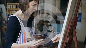 Young painter girl in apron painting still life picture on canvas in art-class