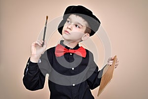 Young painter with red bow tie and black shirt and cap holding paint brush and art palette