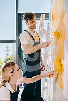 Young painters painting wall in yellow with paint rollers