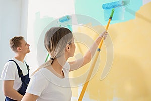 Young painters using rollers for refurbishing color of wall indoors