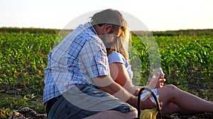 Young pair with white wine glasses resting on corn field at sunset. Family having picnic at nature on summer day. Happy