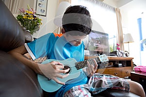 Young pan asian boy practising on his blue ukelele in a home environment