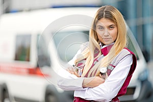 Young paramedic female with phonendoscope at emergency car background