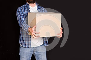 Young parcel delivery man holding a cardboard box in his hands on a black background