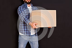 Young parcel delivery man holding a cardboard box in his hands on a black background