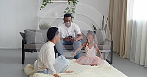 Young parents afro american family spend time with cute active playful daughter in pink dress sitting on sofa at home in