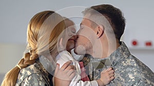 Young parents in camouflage uniform kissing daughter cheek, family closeness