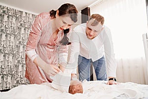 young parents change their newborn baby on a bed in the bedroom.