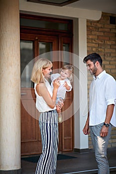 Young parents with child standing front house