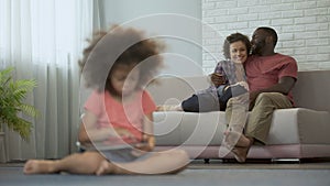 Young parents enjoying joint pastime watching their daughter playing on tablet