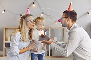 Young parents giving birthday cake to their shy little son during quiet celebration at home