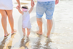 Young Parents Holding by Hands Cute Little Baby Toddler Girl Daughter Learning to Walk. Beach Sea Sunlight. Authentic