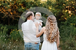 Young parents hugging each other and holding on the hands their little smiling daughter. Concept on family holidays and walking at