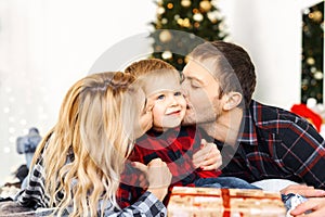 Young parents kissing their son and giving a Christmas present to little boy at Chrismas morning in bed.