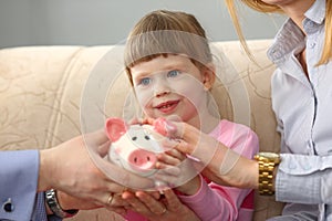 Young parents and little child girl are holding piggy bank