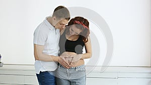 Young parents make the heart hands on the belly of a pregnant woman. Slow motion