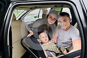 Young parents place baby in rear facing child car seat and tightening safety harness strap.