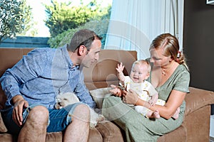 Young parents sitting on the sofa with their cheerful baby and a dog