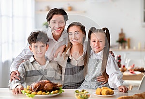 Young parents with son and daughter smiling at camera, cooking Thanksgiving or Christmas dinner with turkey at kitchen