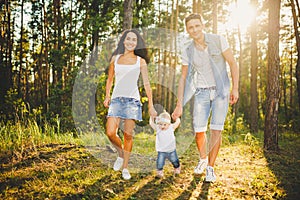 Young parents are taught to walk a daughter of one year on nature in a park on a lawn. The first steps of the child`s hand with