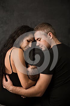 Young parents with their baby on a dark background, back view