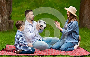 Young parents and their child playing with soccer ball during picnic in countryside