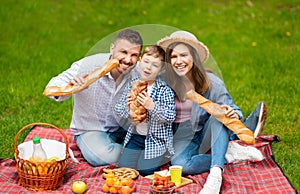 Young parents with their kid eating bread loaves during family picnic in countryside